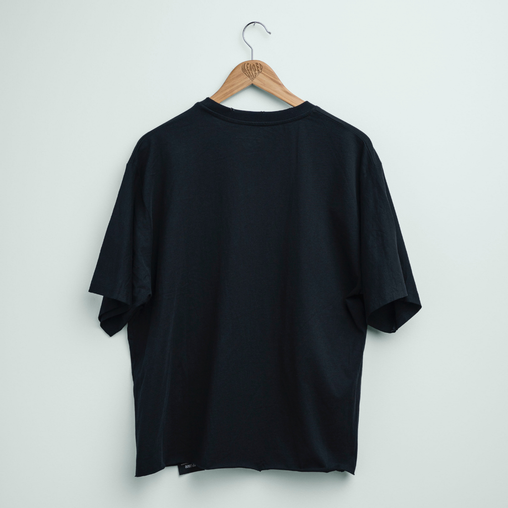 A black short-sleeve crewneck t-shirt hanging on a wooden hanger against a plain light gray wall.