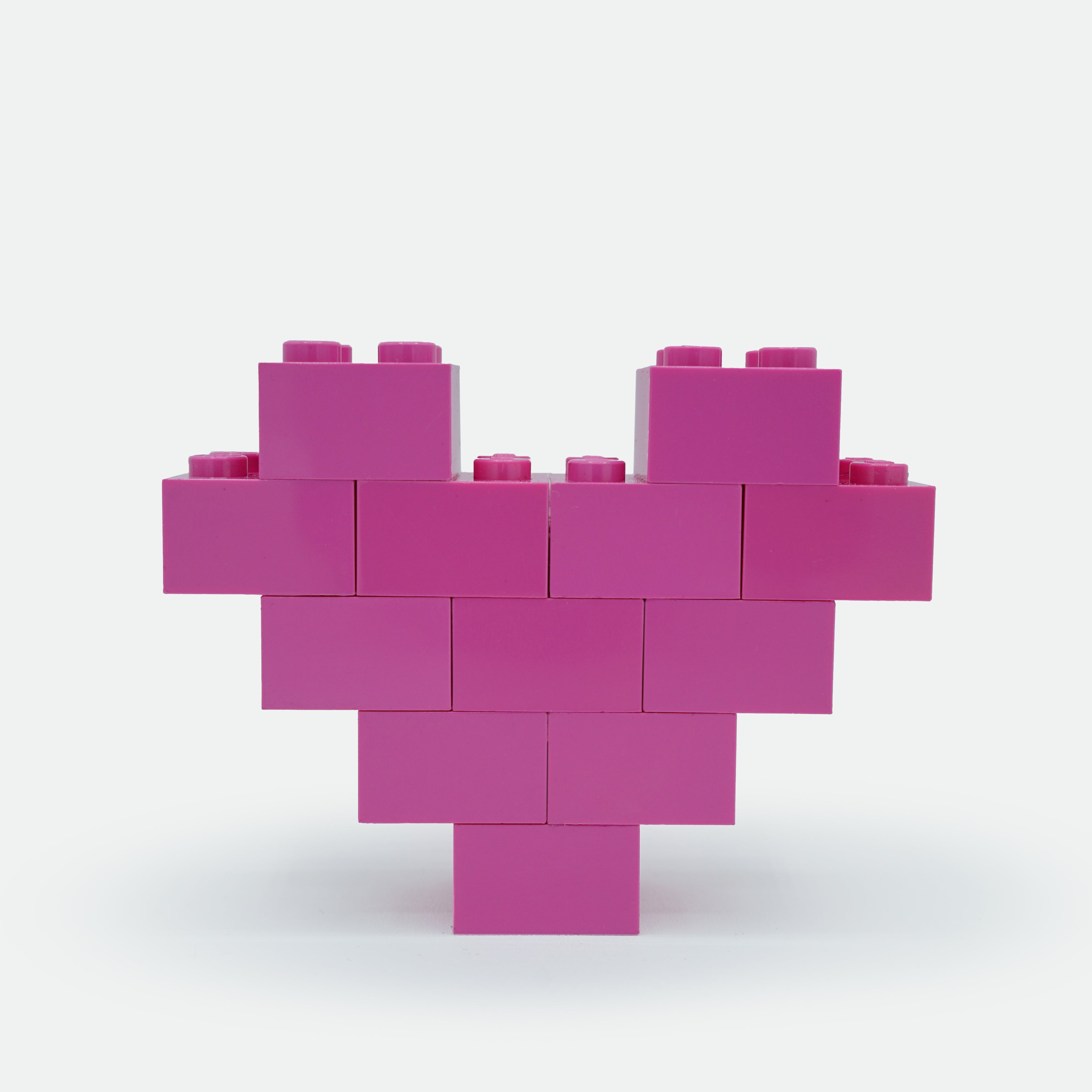Pink heart-shaped structure made of interlocking bricks on a white background