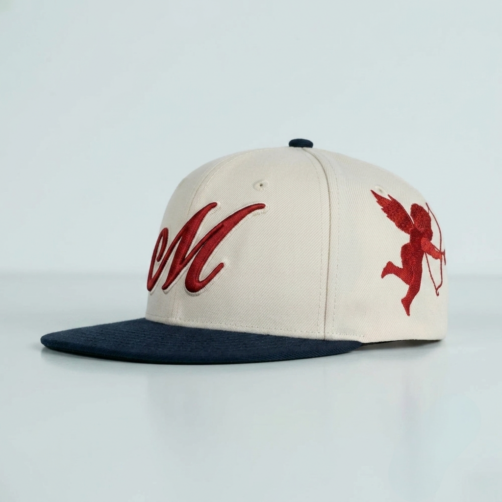 An off-white snapback cap with a dark navy blue flat brim, featuring red embroidered lettering on the front and a red cupid graphic on the side.