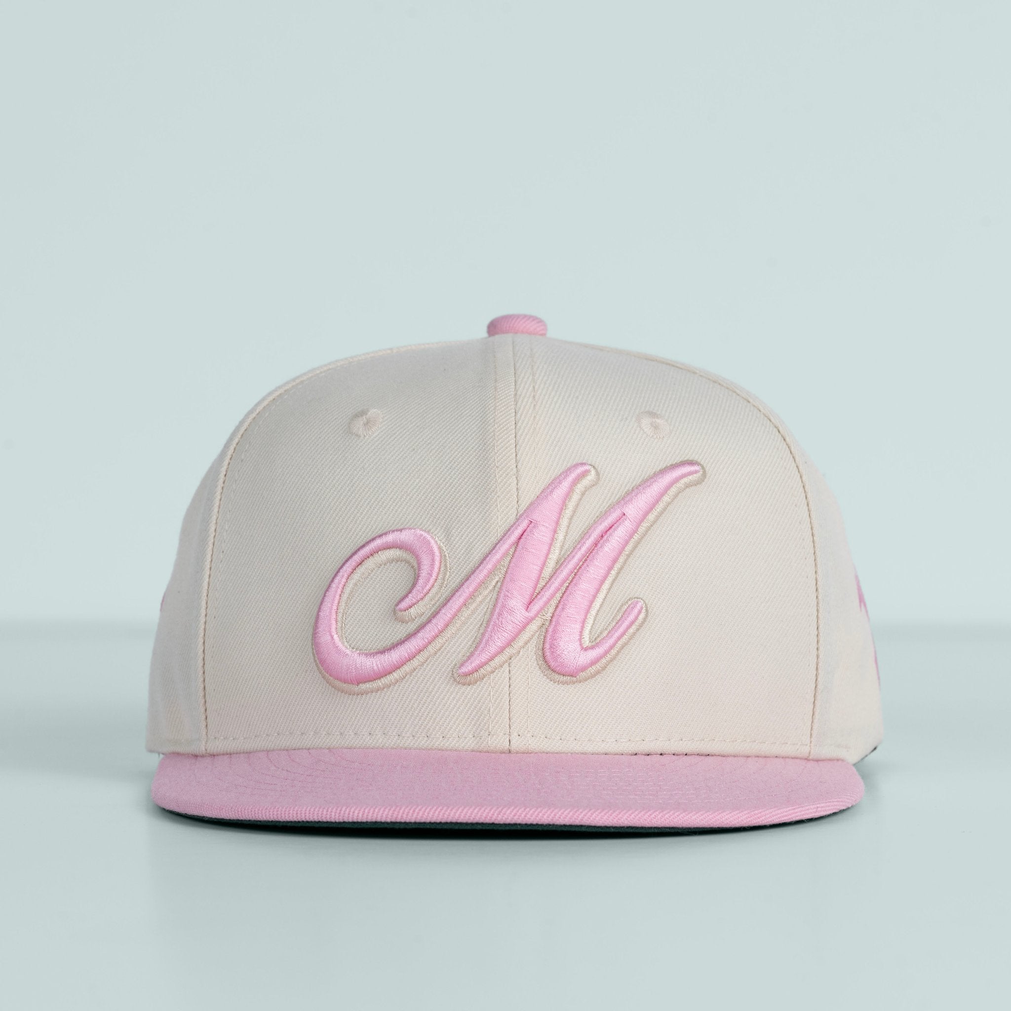 Beige and pink cap with a large 'M' on a light gray background