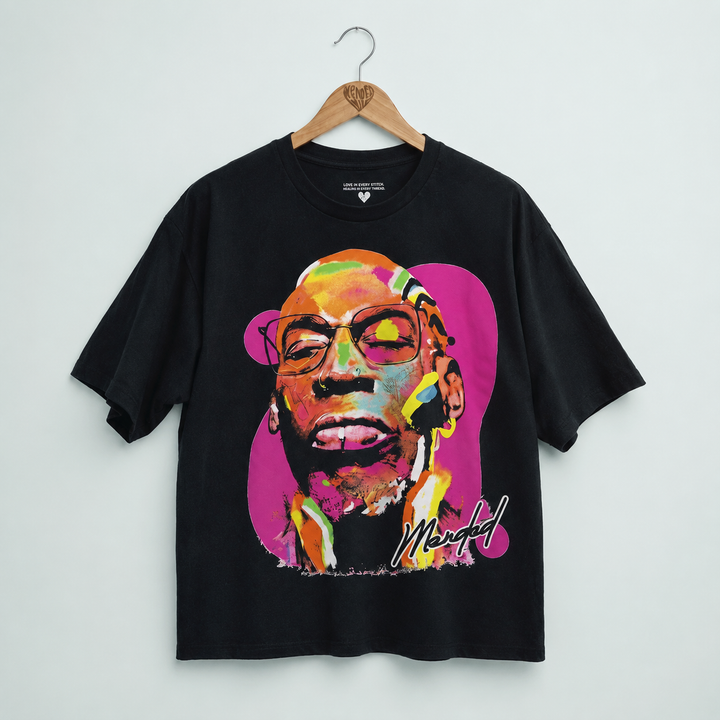 A black short-sleeve graphic T-shirt hanging on a wooden hanger against a light gray wall. The shirt features a large, colorful pop-art style portrait of a man's face with glasses, set against a bright pink circular background, with a stylized signature near the lower right of the graphic.